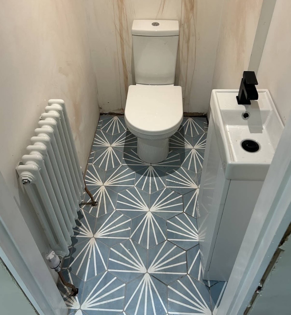 Compact white column radiator installed in a cloakroom toilet with exposed copper pipework.
