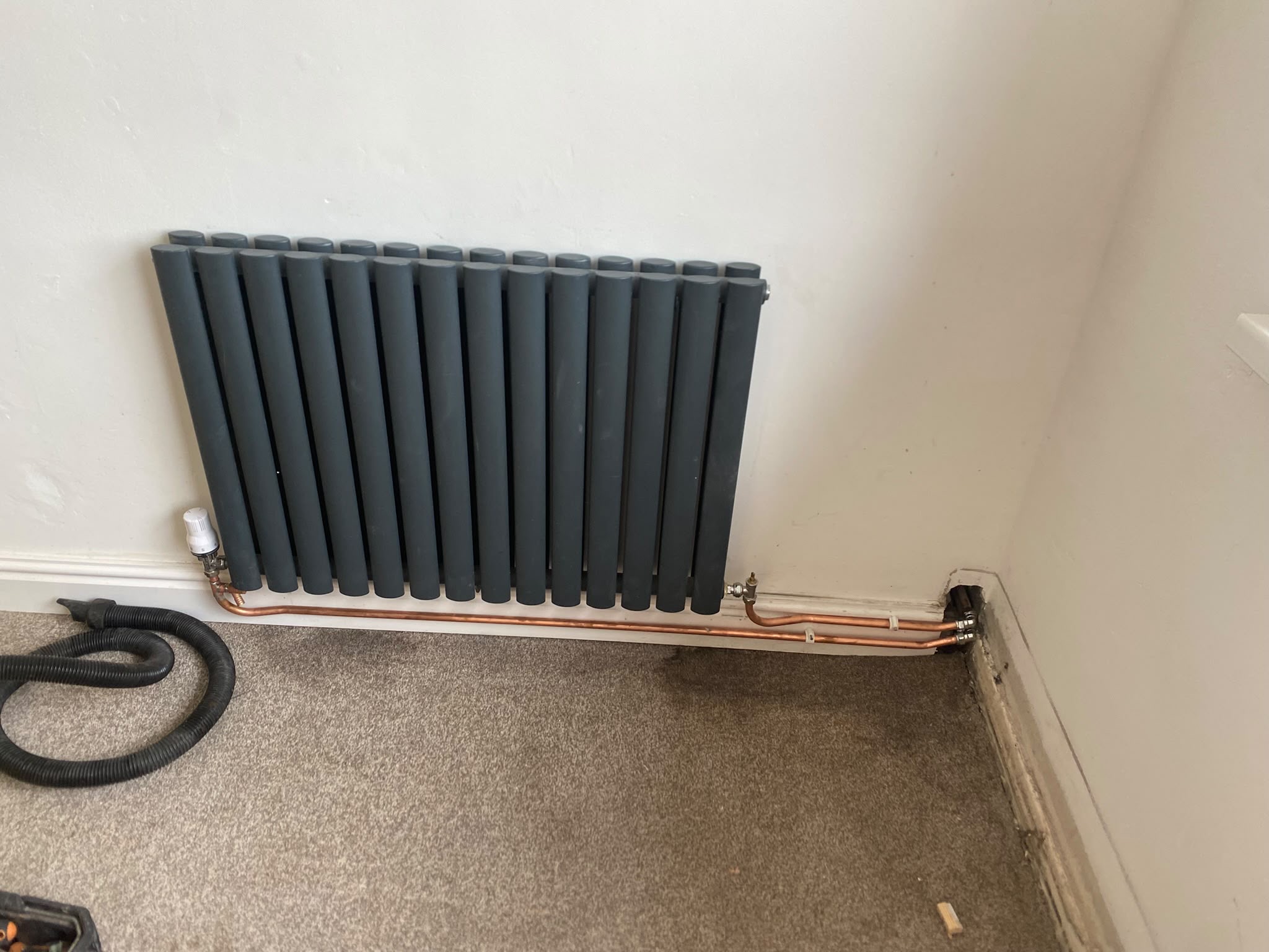 Anthracite horizontal column radiator installed with exposed copper pipework in a Manchester home by Redmond Heating Services.